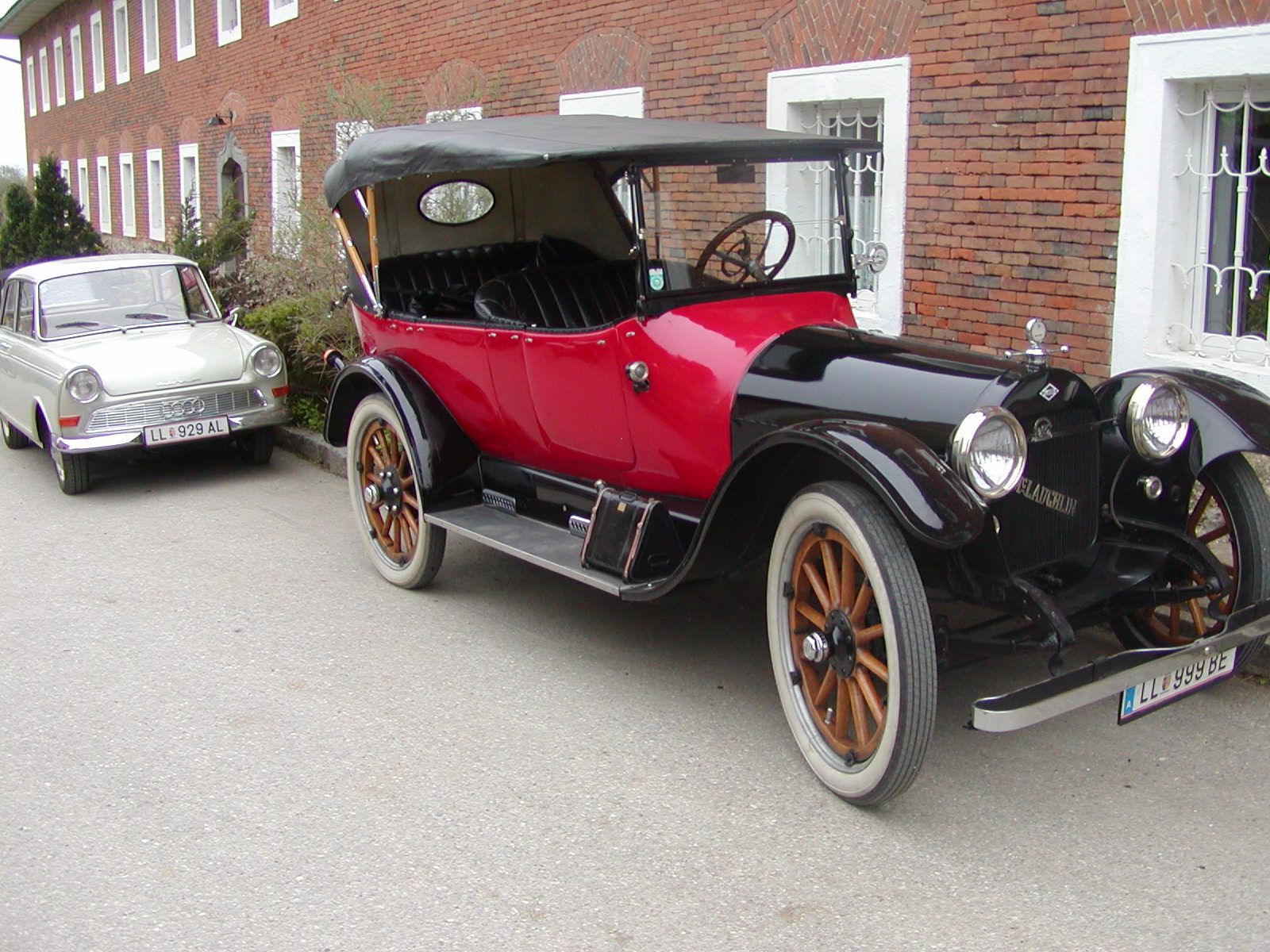 Két oldtimer autó parkol egy téglaépület előtt.