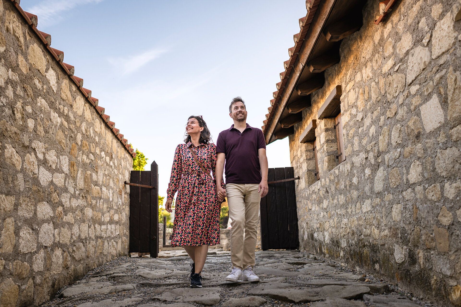 Pár sétál a római kori Carnuntum város római negyedében. Balra és jobbra kőházak. 