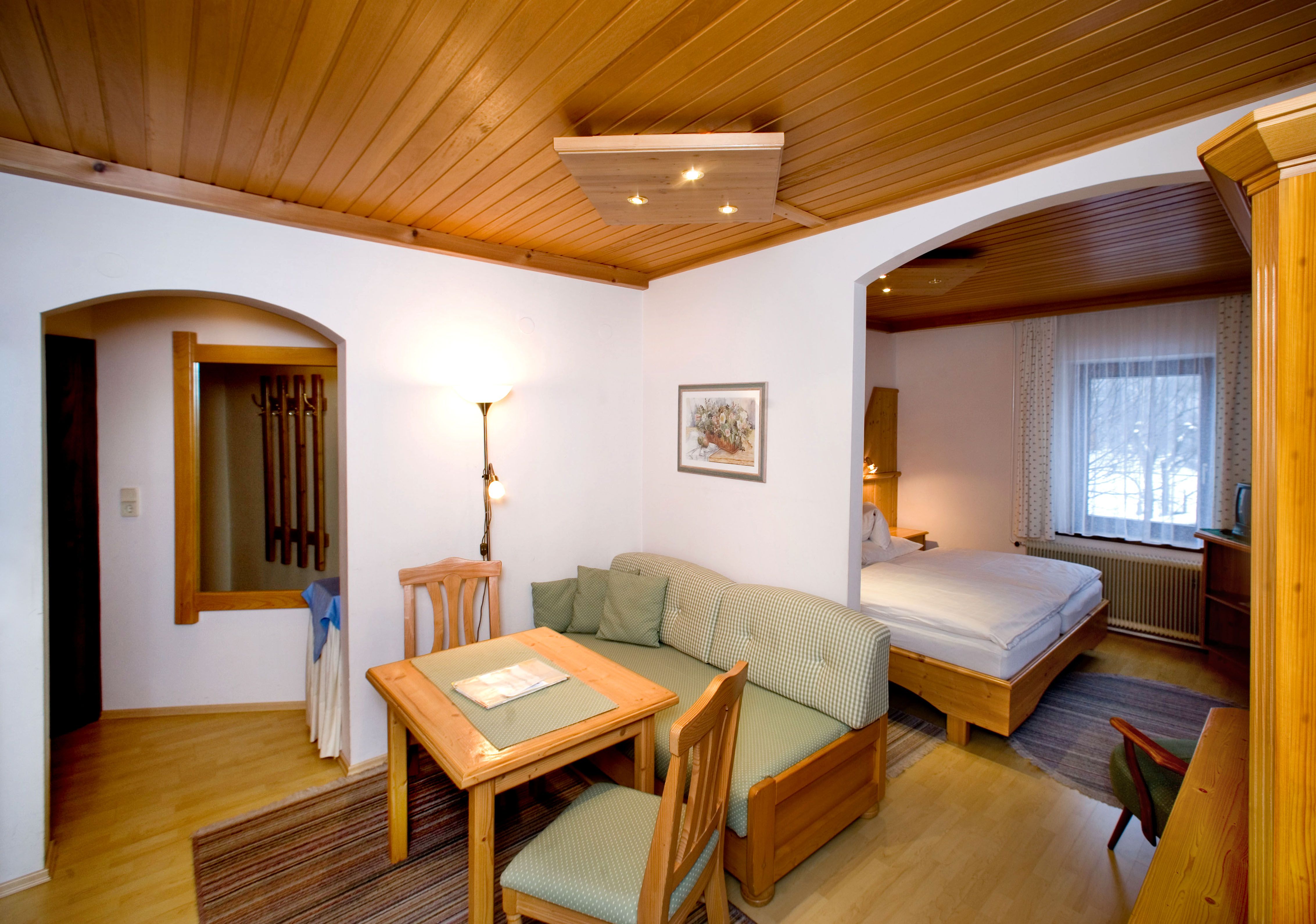 Hangulatos hotelszoba fabútorokkal, étkezőasztallal, kanapéval és franciaággyal.