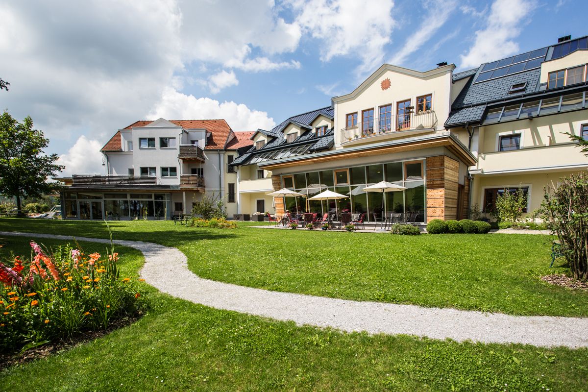 Nagy ház kerttel és terasszal, zöld rétekkel és virágokkal körülvéve.