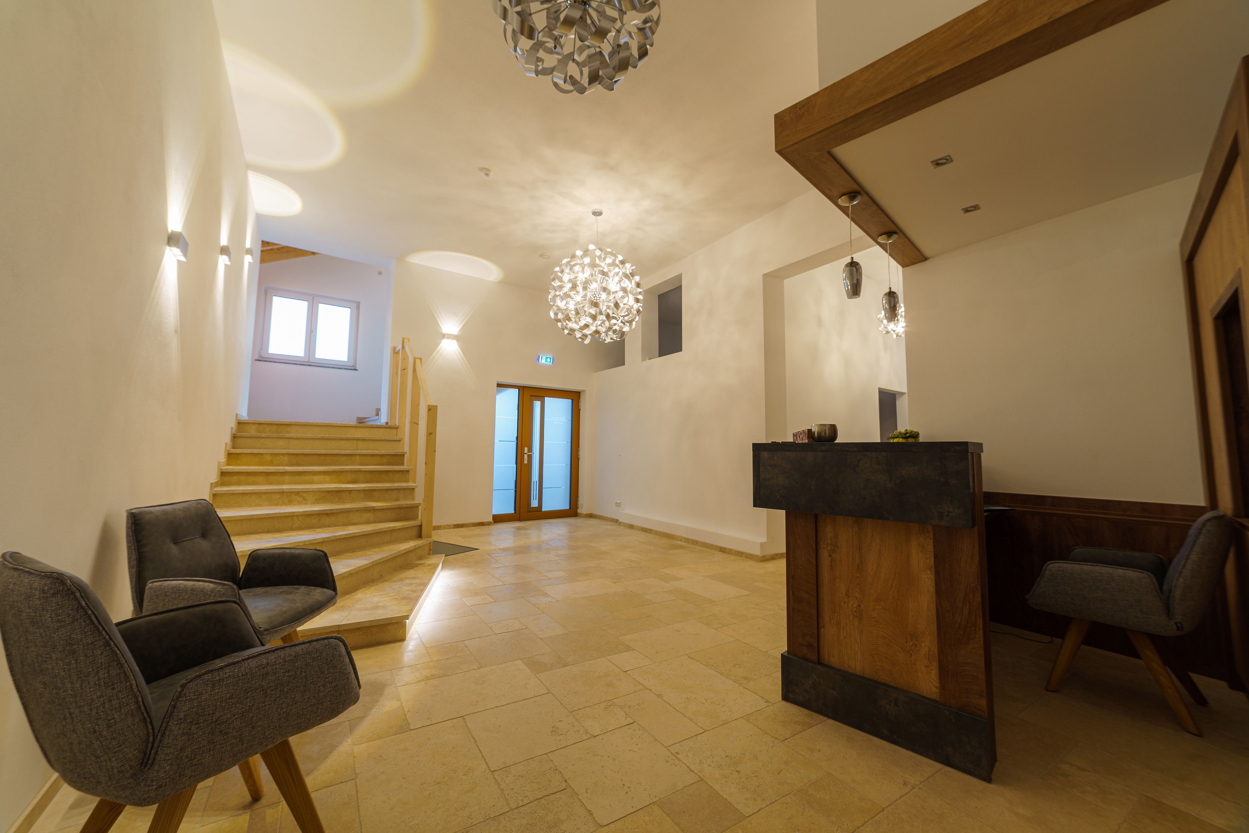 Modern recepció, fapult, két szürke fotel és lépcső.