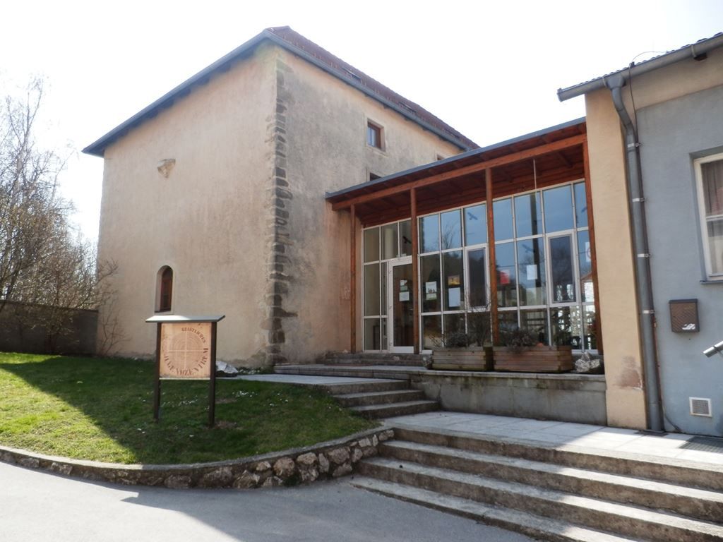 Egy történelmi épület egy modern bővítéssel és egy táblával az előtérben.