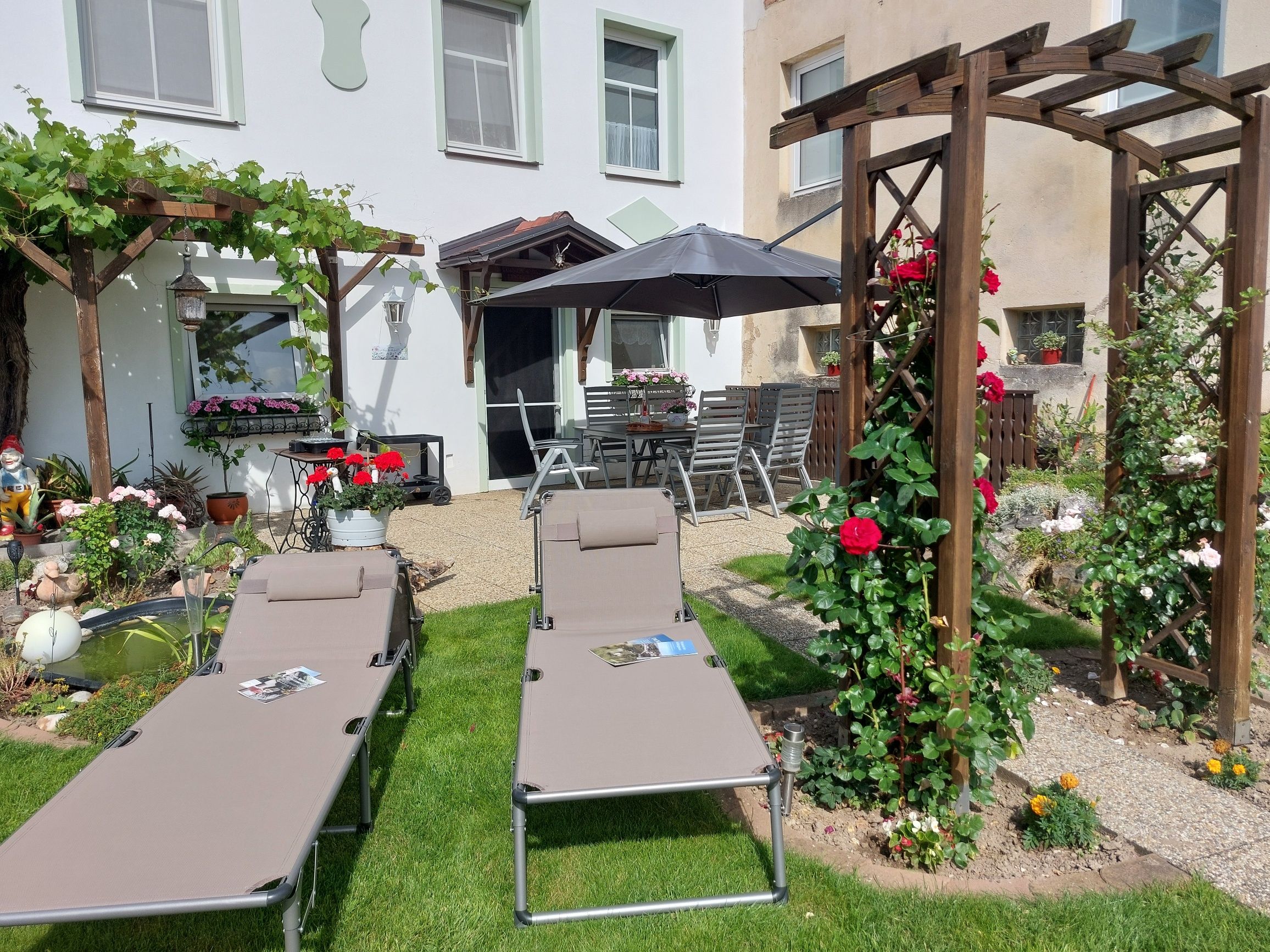 Kert napozóágyakkal, pergolával és virágokkal.