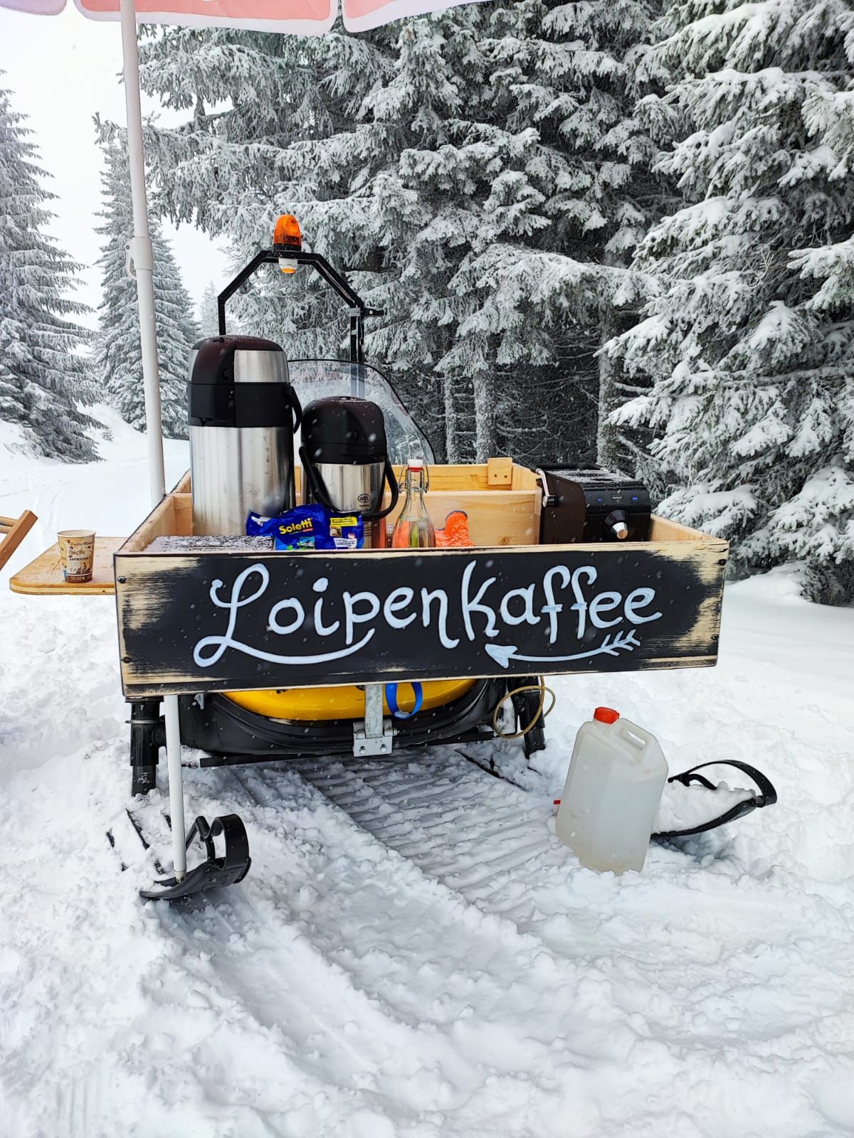 Mobil kávés stand a hóban "Loipenkaffee" felirattal.