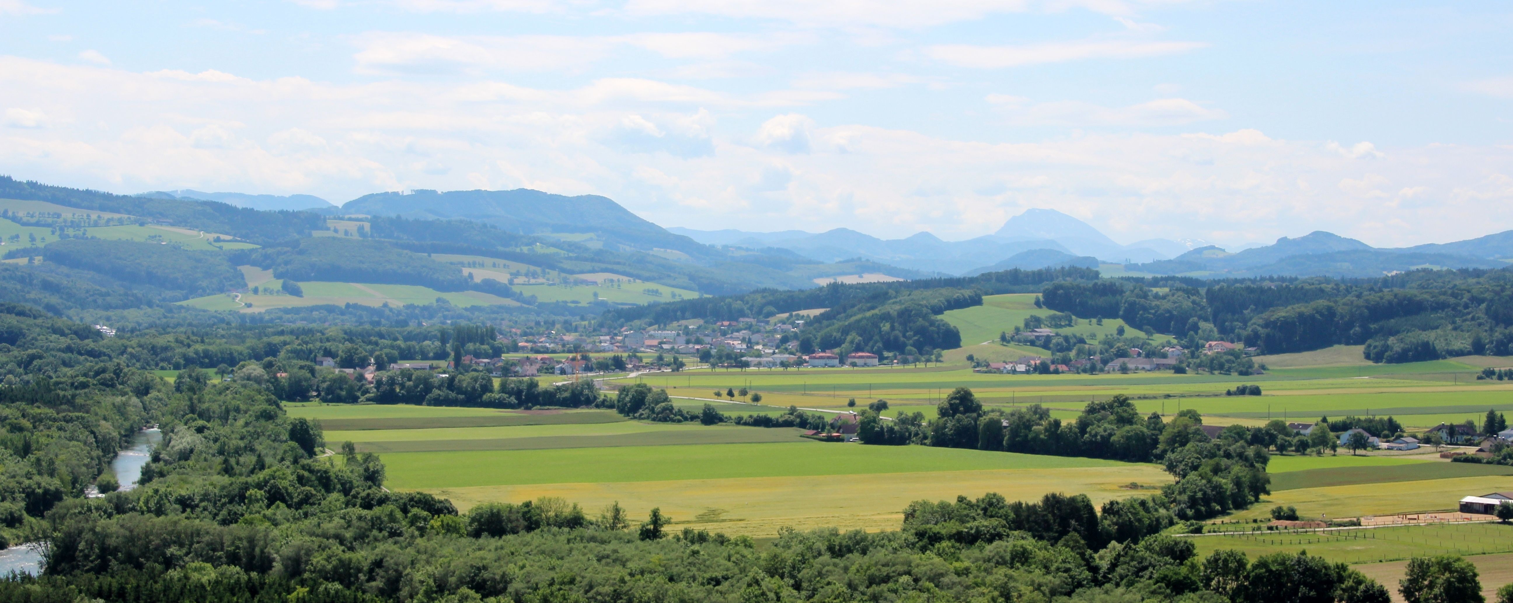 Panoráma egy zöld tájról, dombokkal, mezőkkel és egy folyóval.