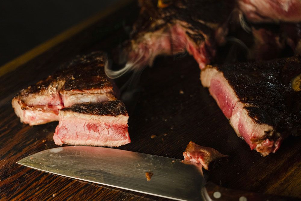 Közelkép egy szeletelt steakről egy fadeszkán, mellette egy késsel.