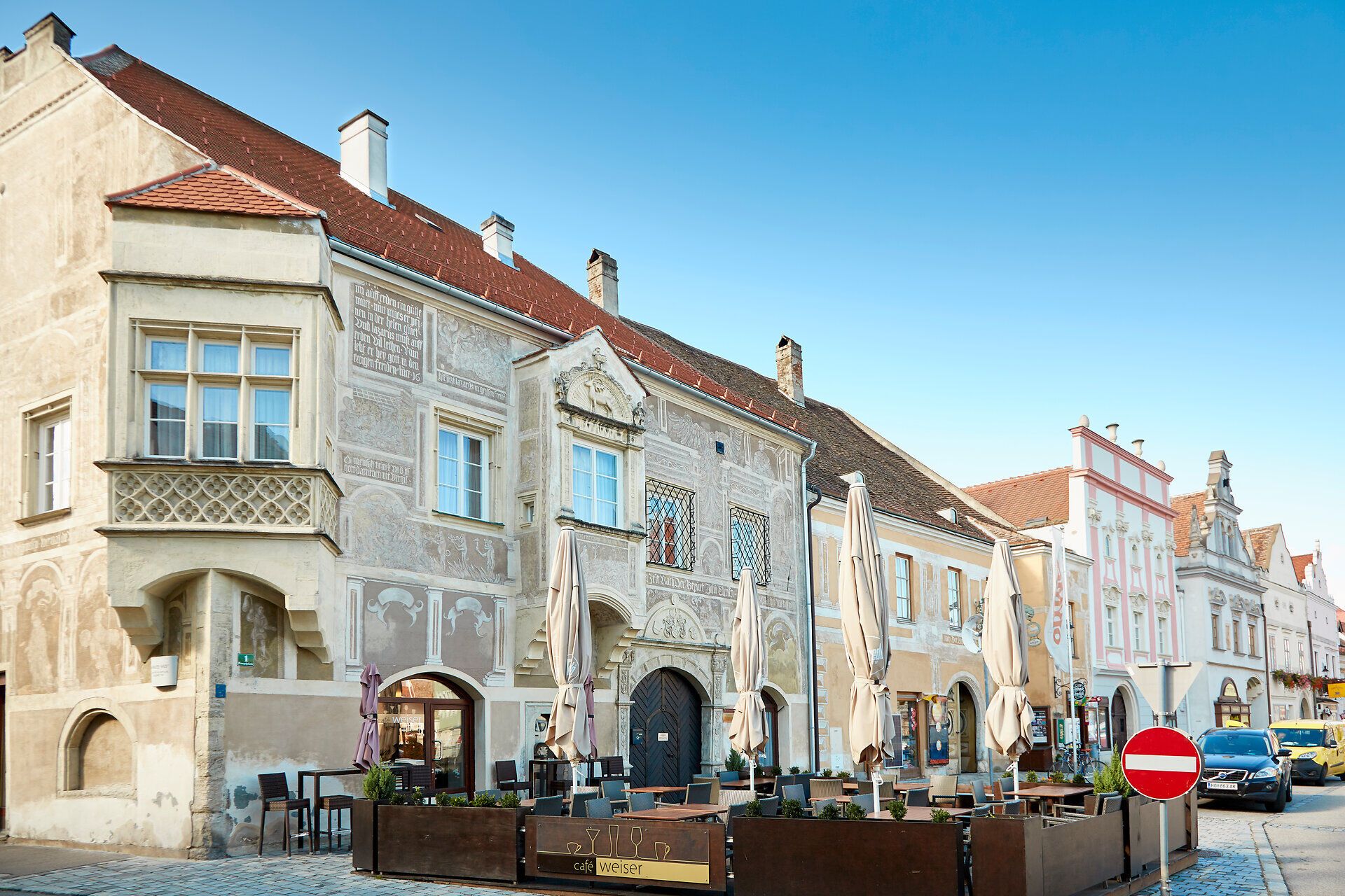 Eggenburg történelmi épületei díszes homlokzatokkal, előtérben egy utcai kávézó.