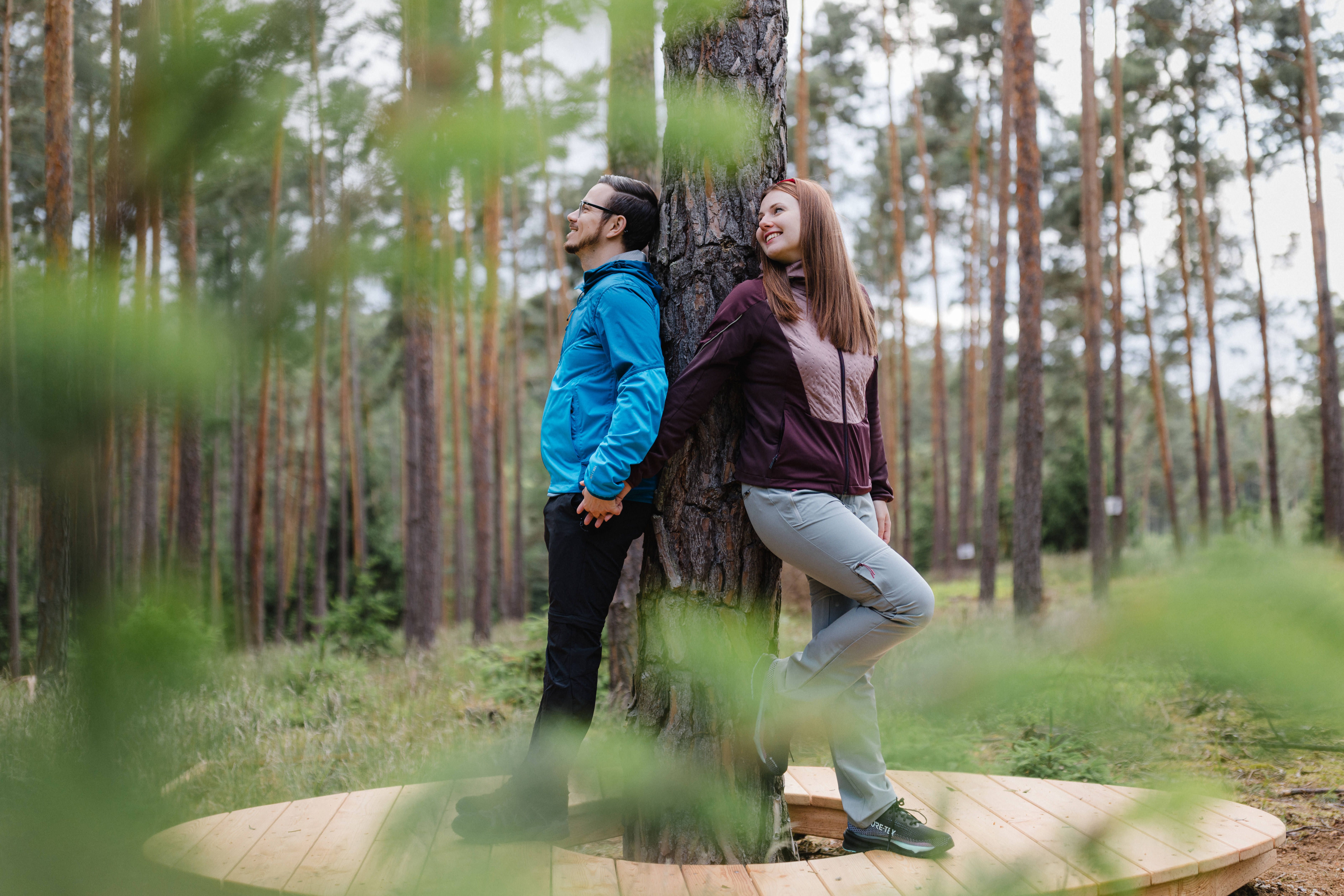 Két ember egy fának támaszkodva az erdőben, egy faplatformon állva.