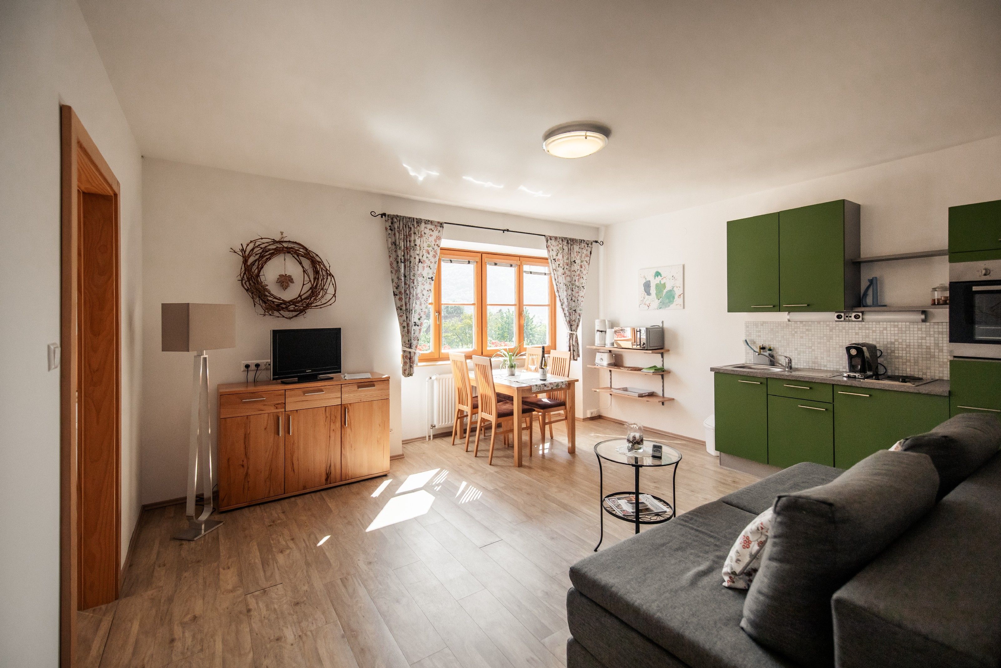 Világos nappali zöld konyhával, étkezőasztallal és kanapéval.