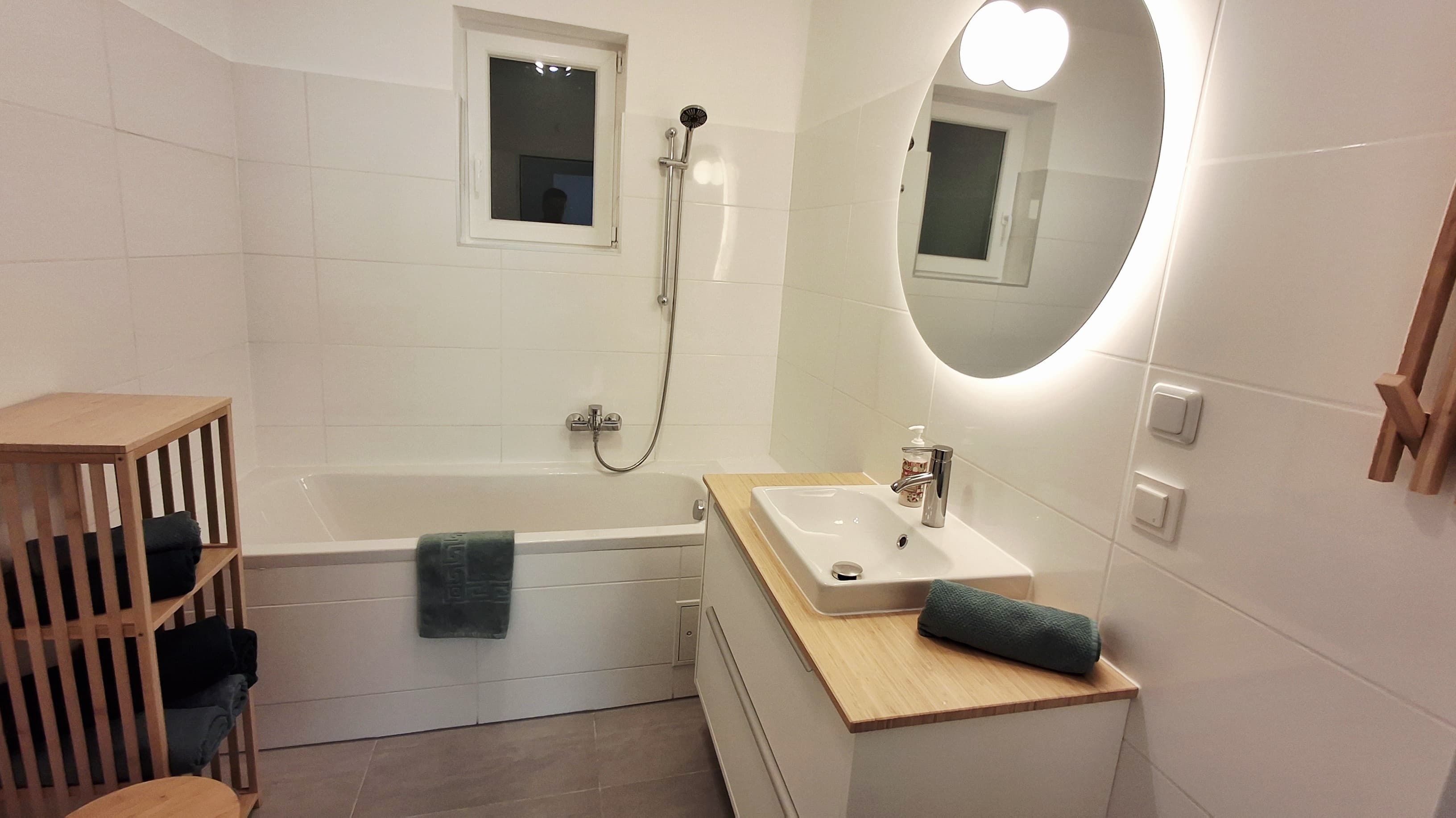 Modern fürdőszoba káddal, mosdókagylóval és világító tükörrel.