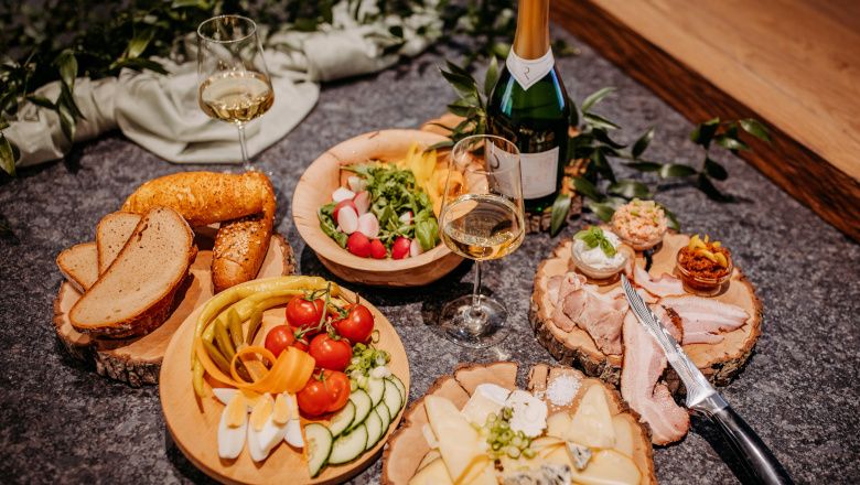 Különböző ételek fatányérokon borosüvegekkel és poharakkal.