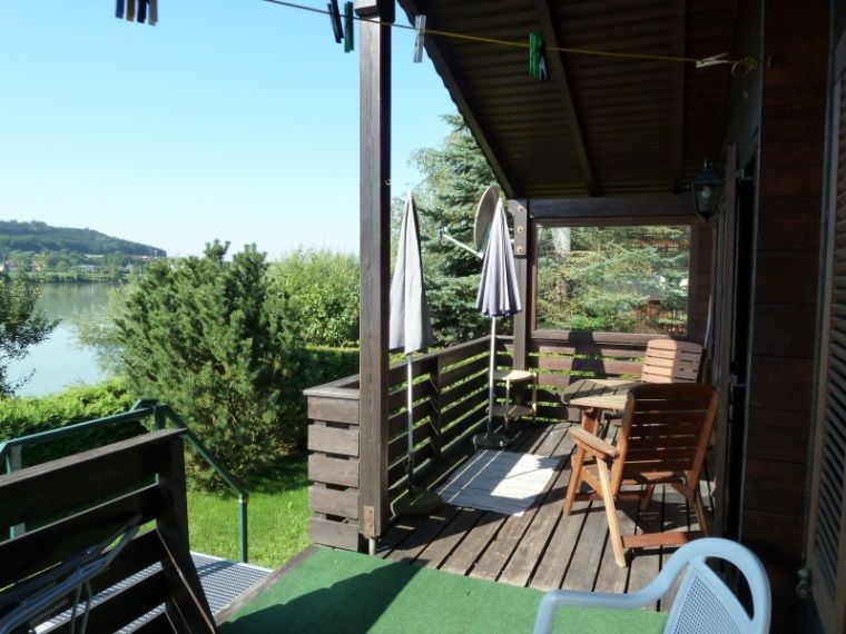 Egy nyaraló fából készült terasza, kilátással a tóra és a zöld tájra.