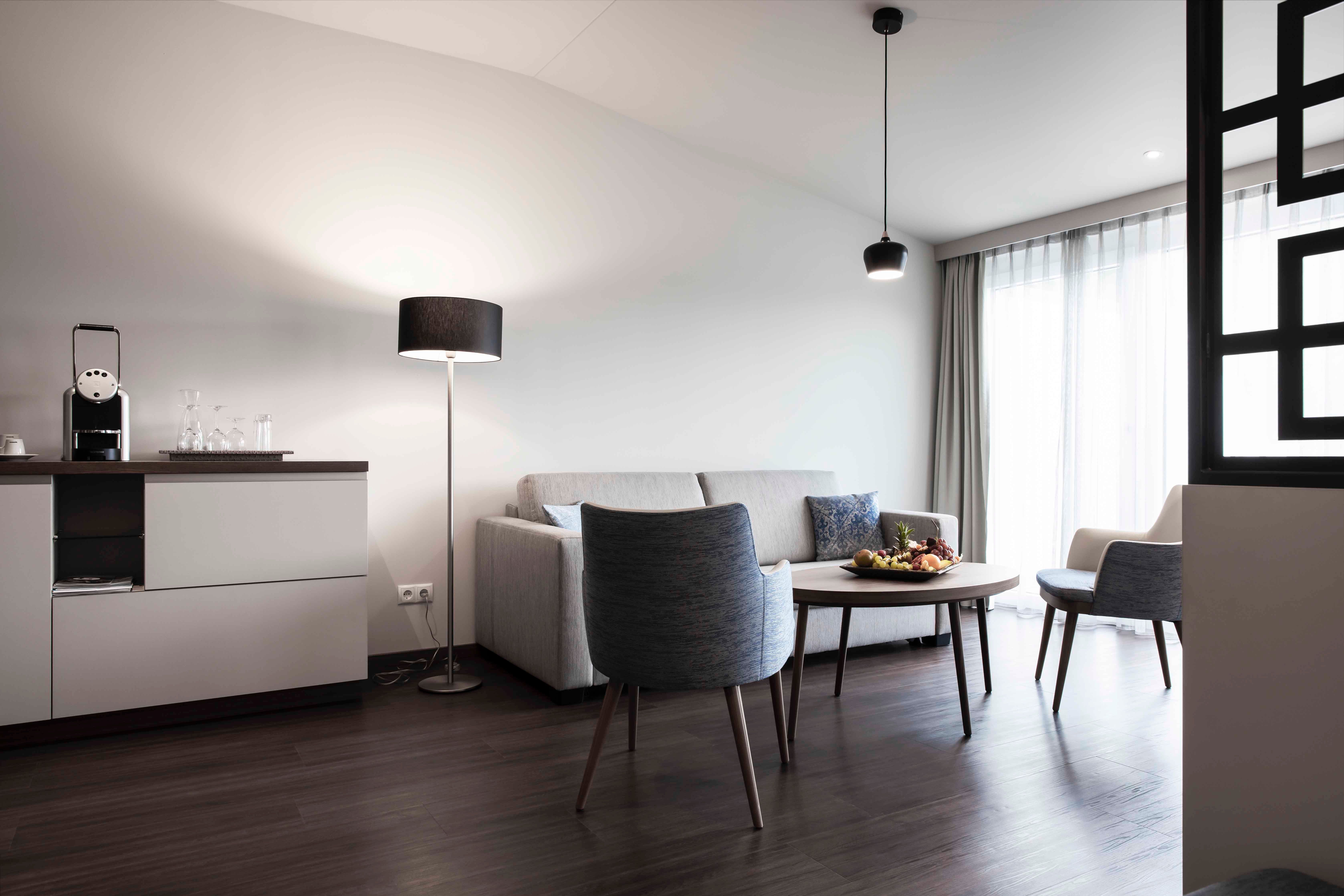 Modern ülősarok kanapéval, karosszékkel, asztallal és állólámpával egy világos szobában.