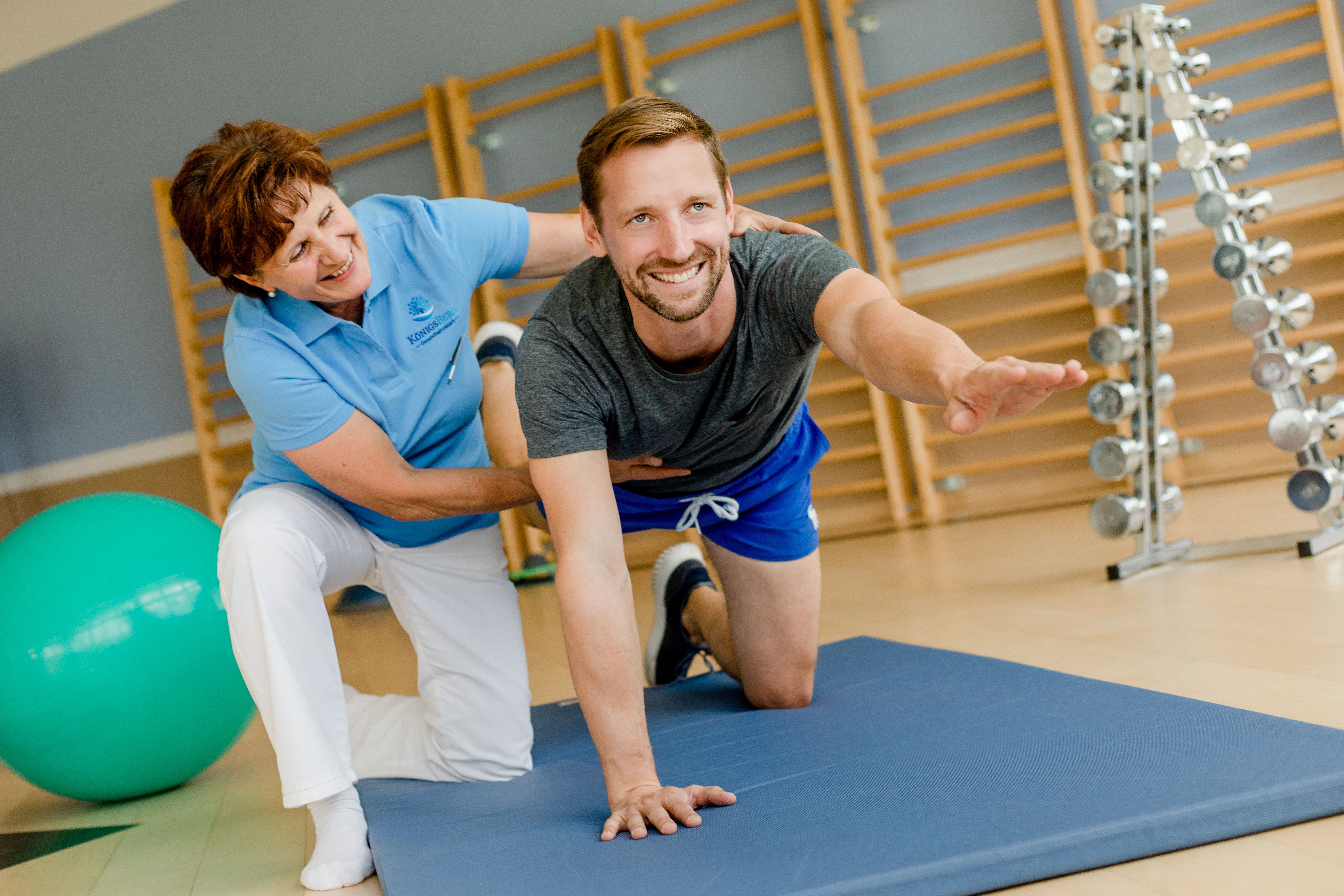 Egy férfi tornagyakorlatot végez egy szőnyegen, egy terapeuta támogatásával egy fitneszteremben.