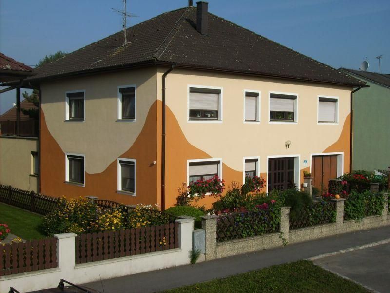Kétszintes ház narancs-bézs homlokzattal és kerttel.