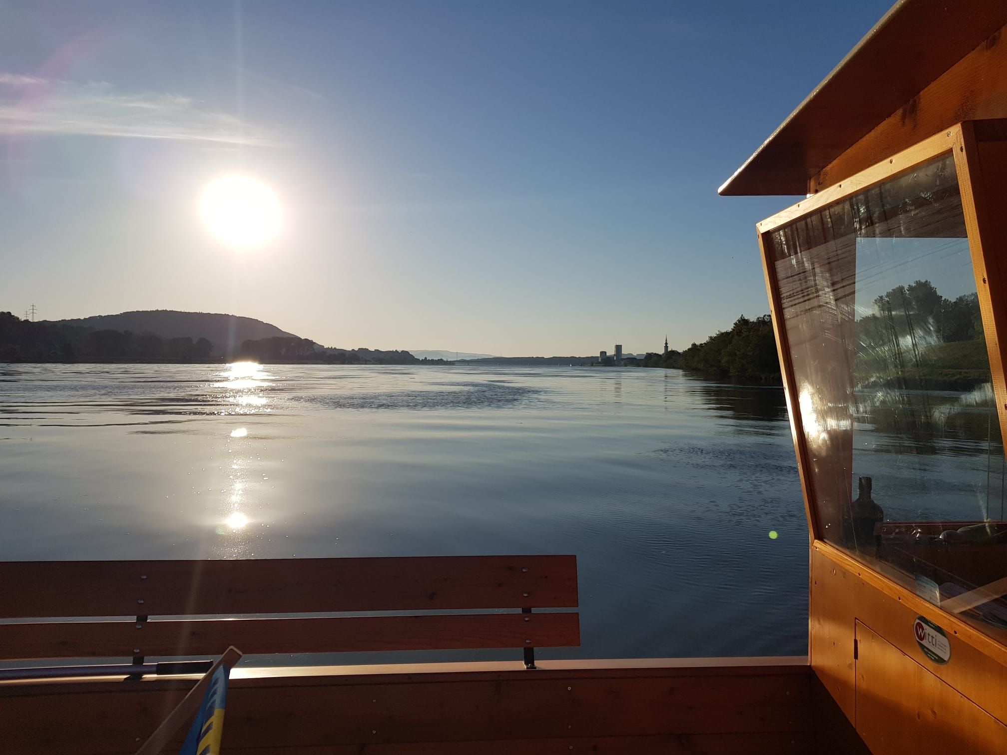 Naplemente egy nyugodt folyó felett, előtérben egy fából készült csónakkal.