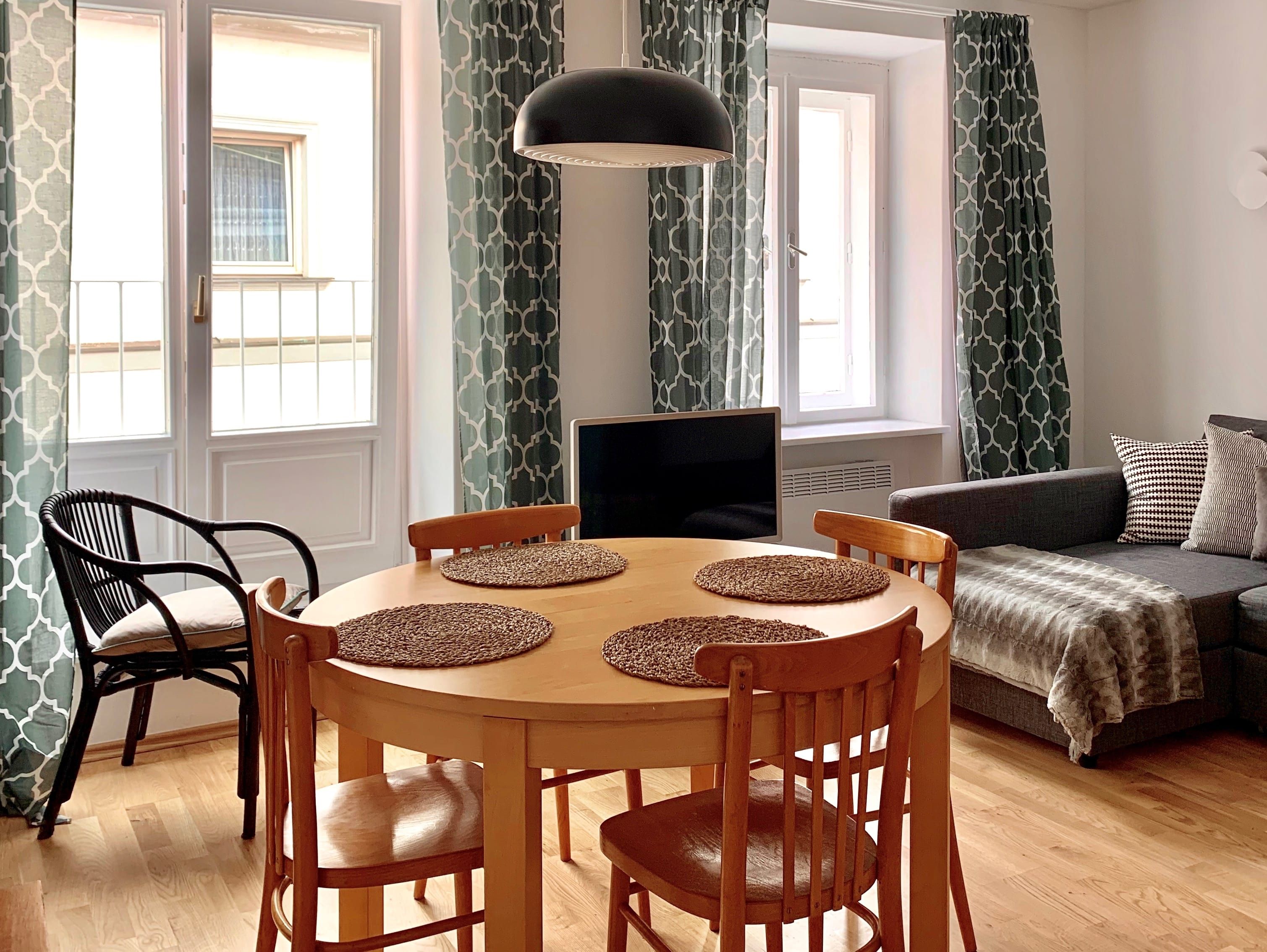 Nappali étkezőasztallal, székekkel, kanapéval és függönyökkel.