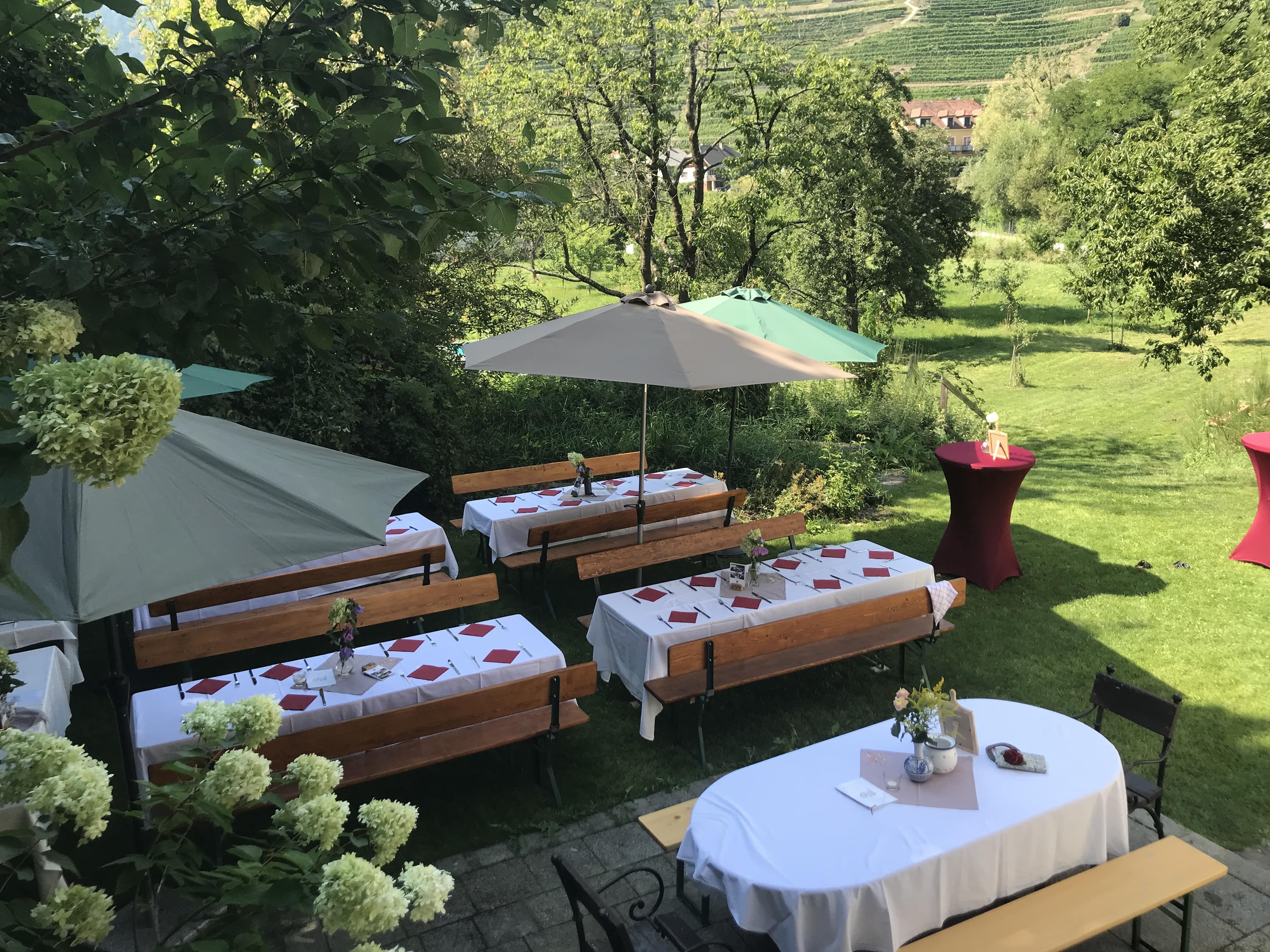 Ünnepélyesen megterített szabadtéri asztalok napernyőkkel és virágdíszekkel.