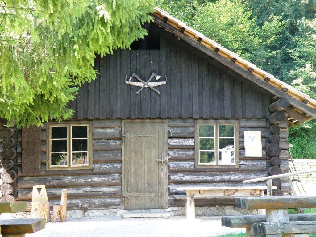 Fából készült kunyhó két ablakkal és egy ajtóval, fákkal körülvéve.