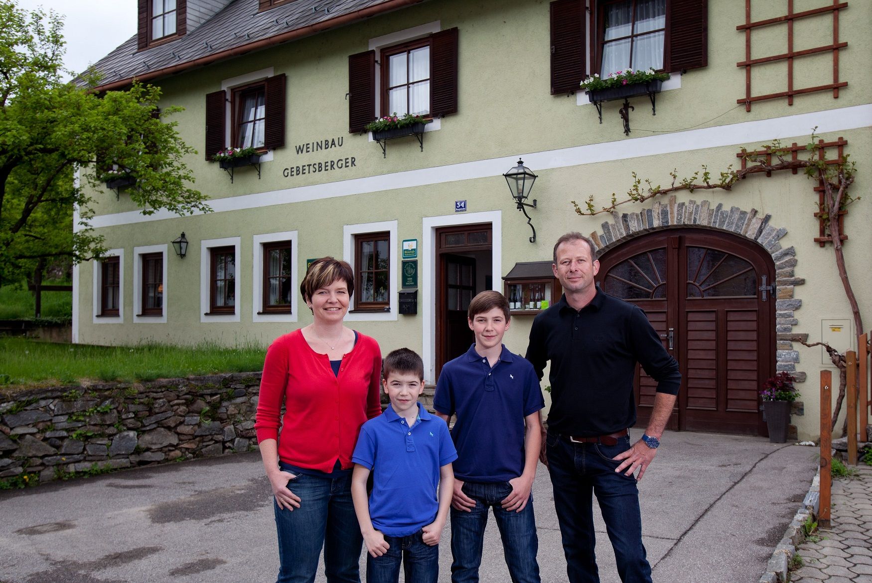 Egy család áll a "Weinbau Gebetsberger" feliratú épület előtt.
