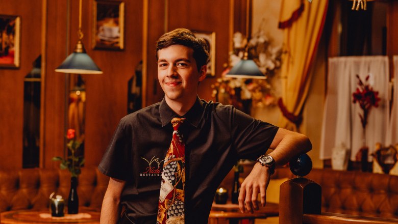 Fiatal férfi egy étteremben, nyakkendőben és ingben, mosolyogva.