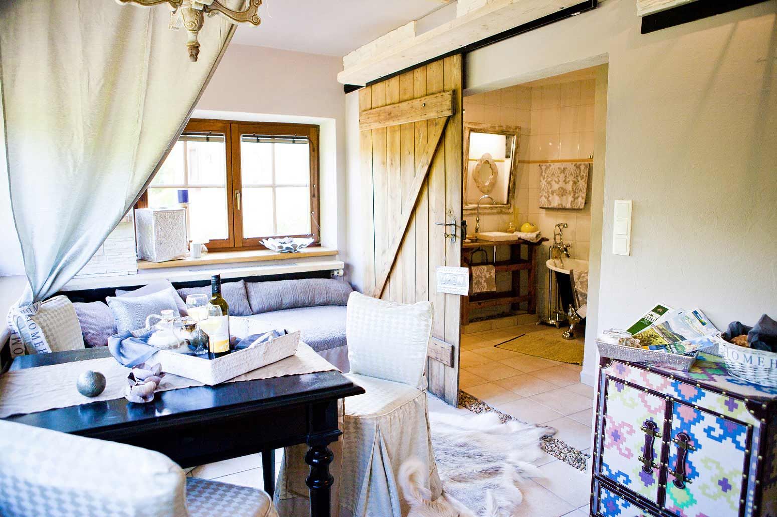 Hangulatos nappali faajtóval, kanapéval, asztallal és dekorációs elemekkel, kilátás a fürdőszobába.