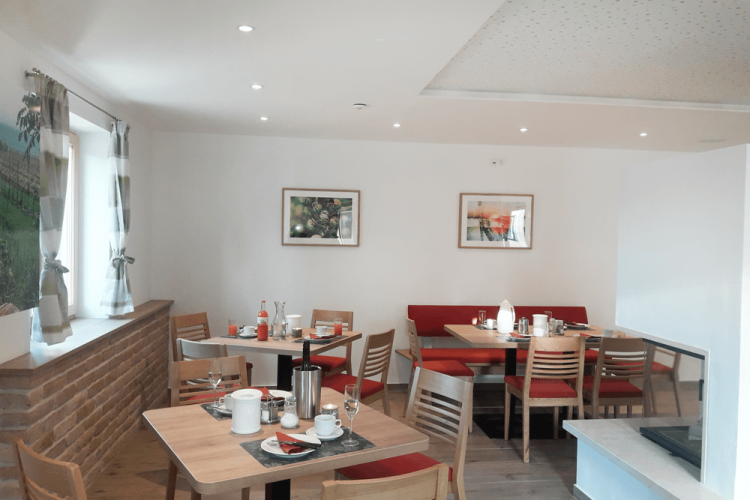 Hangulatos reggelizőterem, faasztalokkal, piros kárpitozott padokkal és dekoratív faliképekkel.