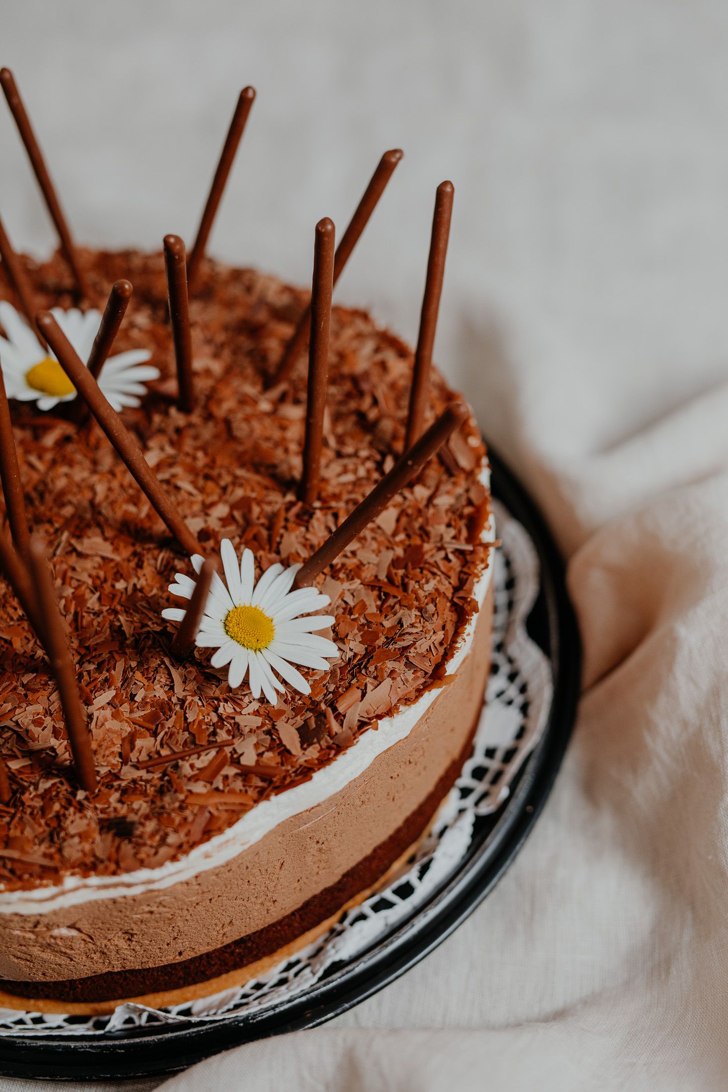 Csokoládétorta csokoládé rudacskákkal és százszorszépekkel díszítve.