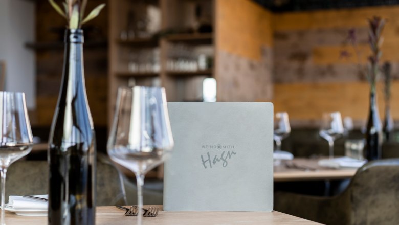 Egy megter&iacute;tett asztal egy &eacute;tteremben borospoharakkal, egy &uuml;veg borral &eacute;s egy &eacute;tlappal.